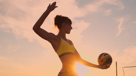 A-beautiful-woman-in-a-bikini-with-a-ball-at-sunset-is-getting-ready-to-do-serve-jump-on-the-beach-in-a-volleyball-match-on-the-sand.-The-decisive-moment-the-tense-moment-of-the-match-in-slow-motion.